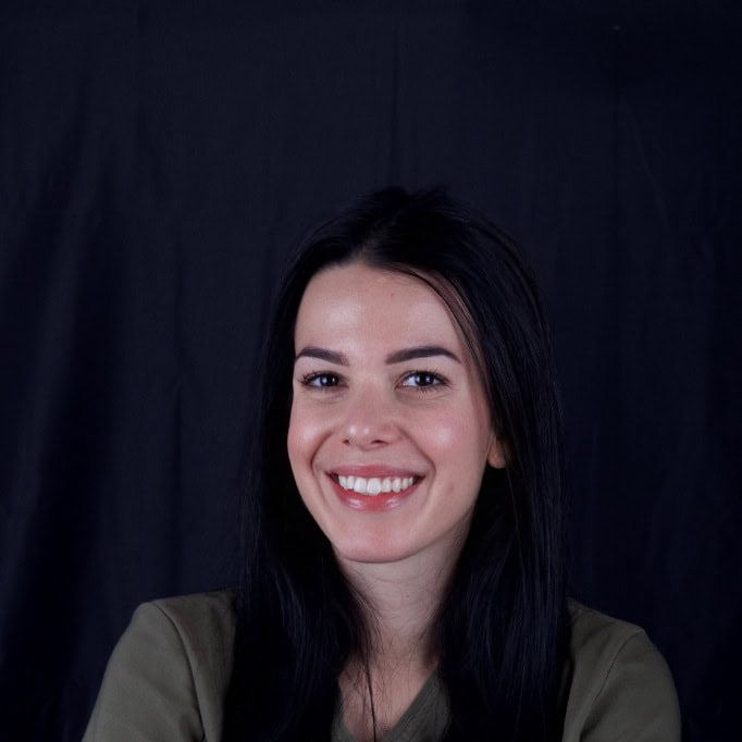 Smiling woman with long dark hair posing against a black backdrop (portrait).